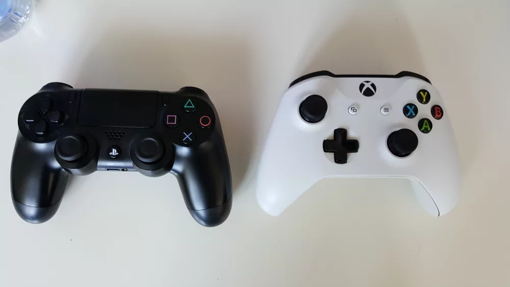 Melns PlayStation DualShock 4 un balts Xbox One kontrolieris blakus
